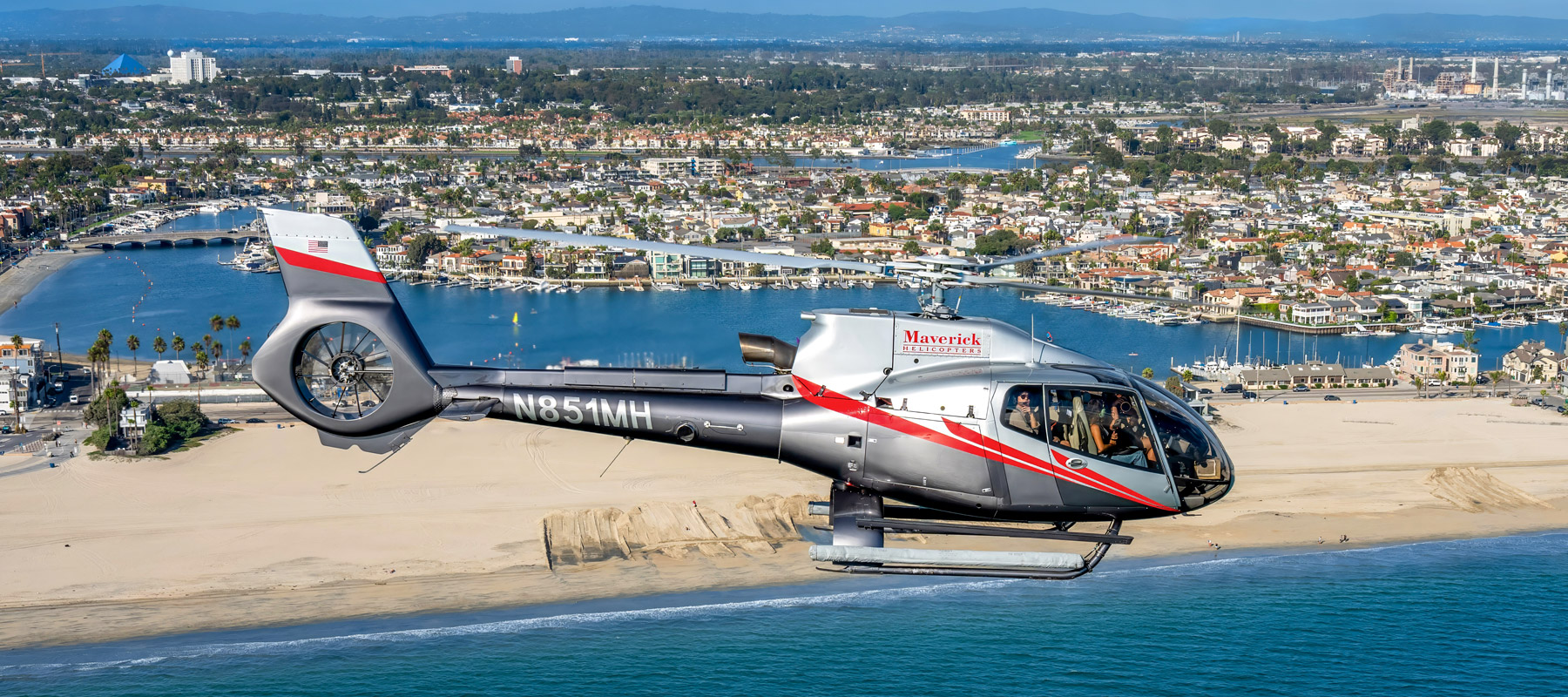 Maverick Helicopters aircraft flying over a Southern California beach and coastal harbor